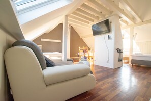 A modern loft bedroom with a sloped ceiling, a flat-screen TV mounted on the wall, and a cozy seating area with a sofa and a chair. - Lovely City House (Meerbusch)