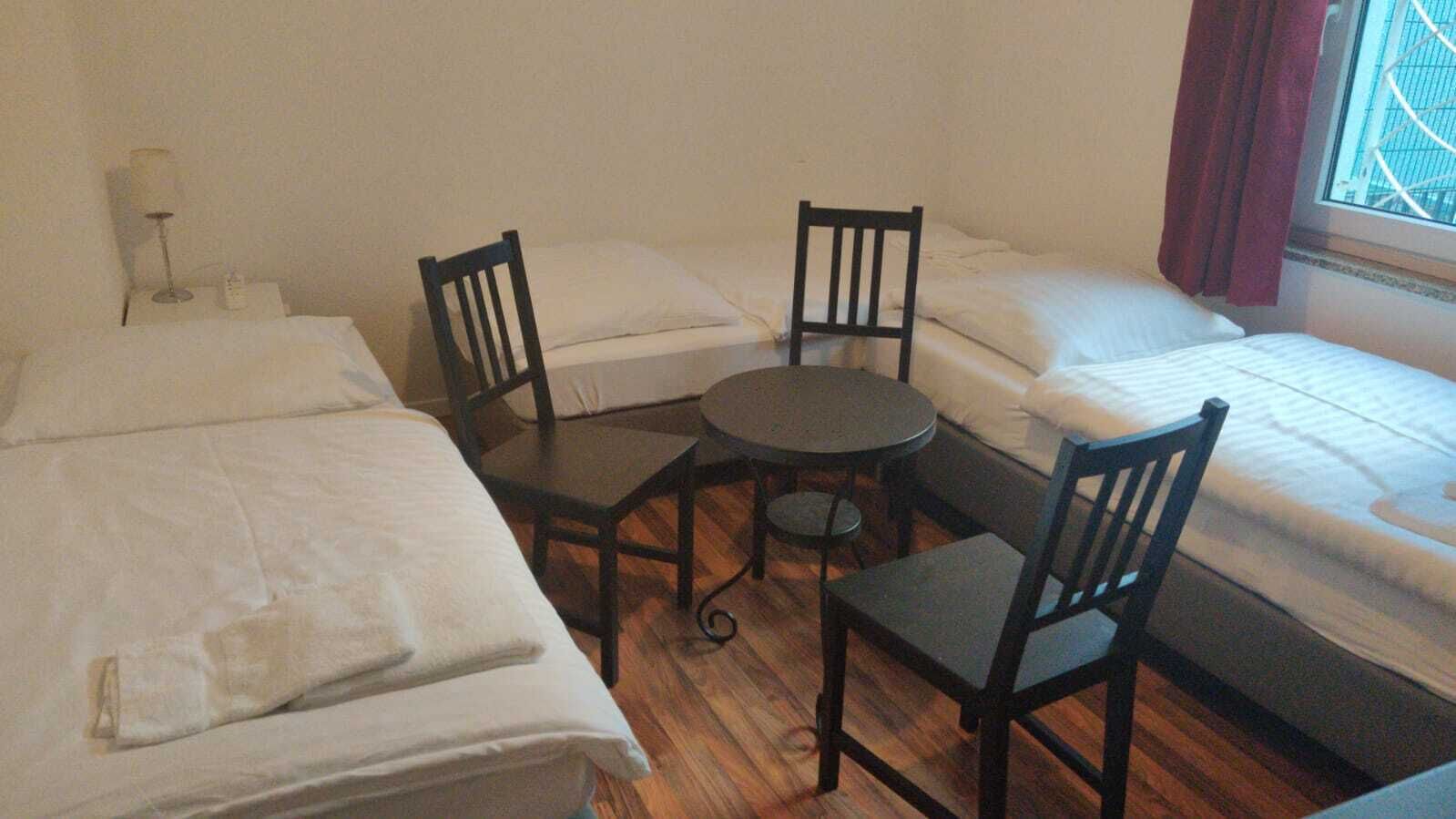 Ein kleiner, kompakter Raum mit drei Einzelbetten, einem runden Tisch und zwei Stühlen.