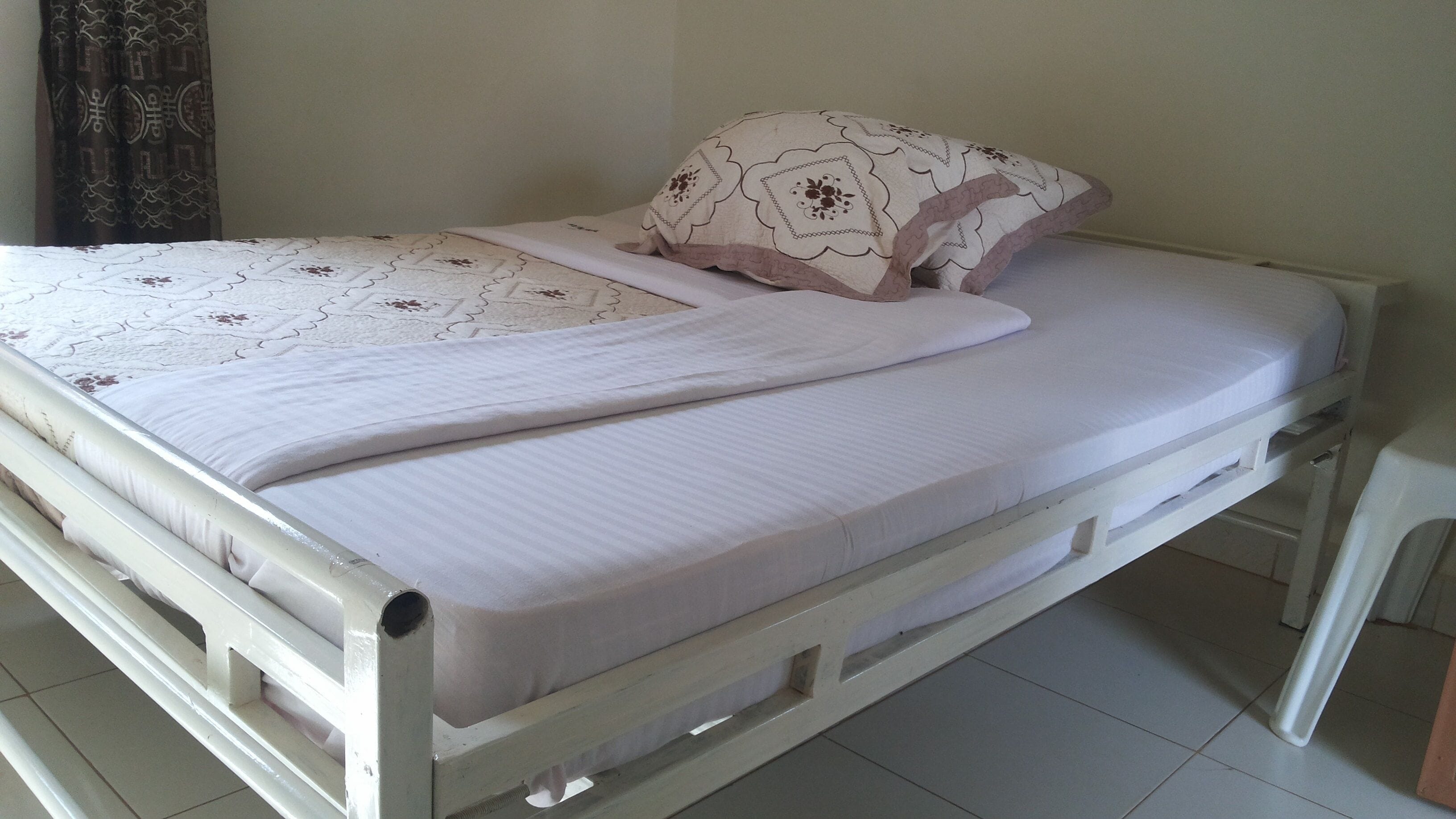 Un lit simple avec un matelas blanc et une couverture à motifs, un oreiller orné de motifs floraux et un mur uni en arrière-plan.