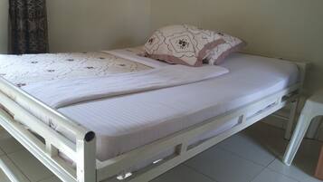 Un lit simple avec un matelas blanc et une couverture à motifs, un oreiller orné de motifs floraux et un mur uni en arrière-plan.