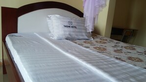 Una cama de hotel con una colcha blanca y un cojín con el logotipo del Hotel Tasha.
