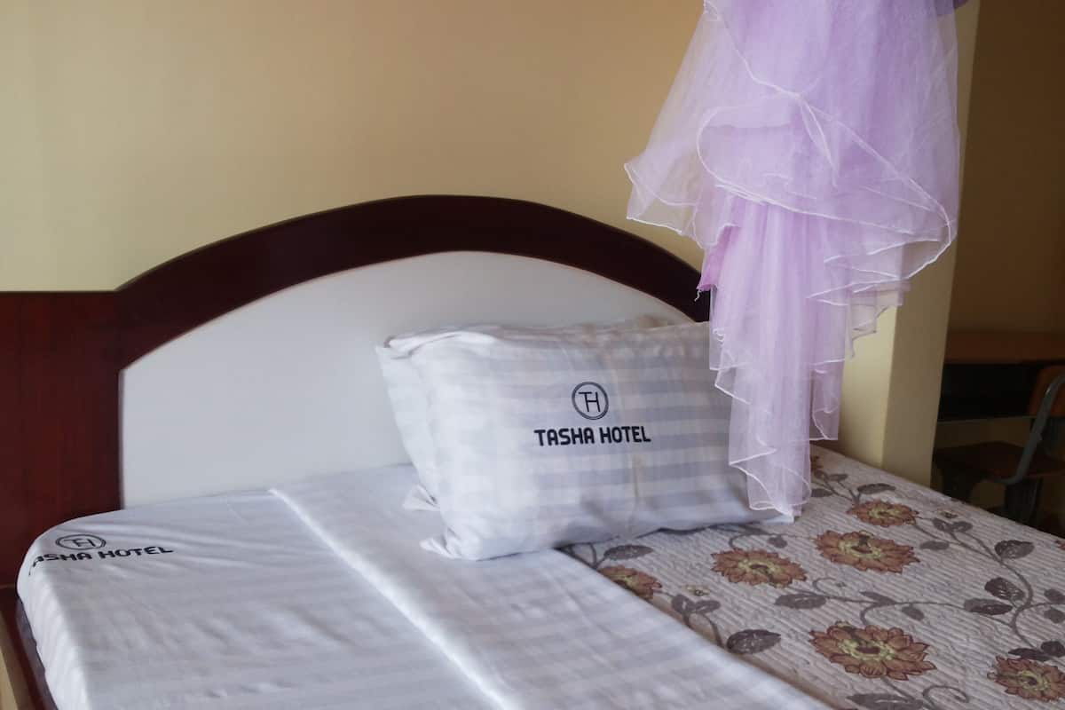 Una cama con un almohadón blanco que dice "TASHA HOTEL" y una colcha de estampado floral.