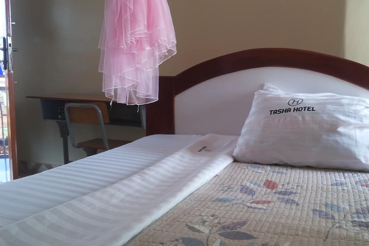 Una habitación de hotel con cama, almohada con el nombre del hotel, mesita de noche y una silla.