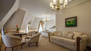 A spacious loft bedroom with a large bed, a sofa, two armchairs, a chandelier, and a painting on the wall. - Residence City Garden (Plovdiv)
