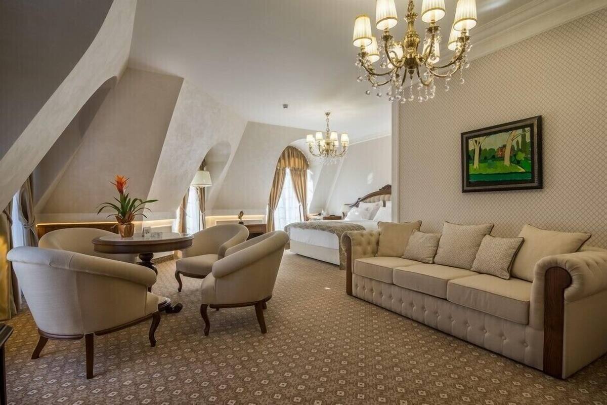 A spacious loft bedroom with a large bed, a sofa, two armchairs, a chandelier, and a painting on the wall.