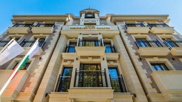 A multi-story hotel building with a central entrance, balconies, and flags. - Residence City Garden (Plovdiv)
