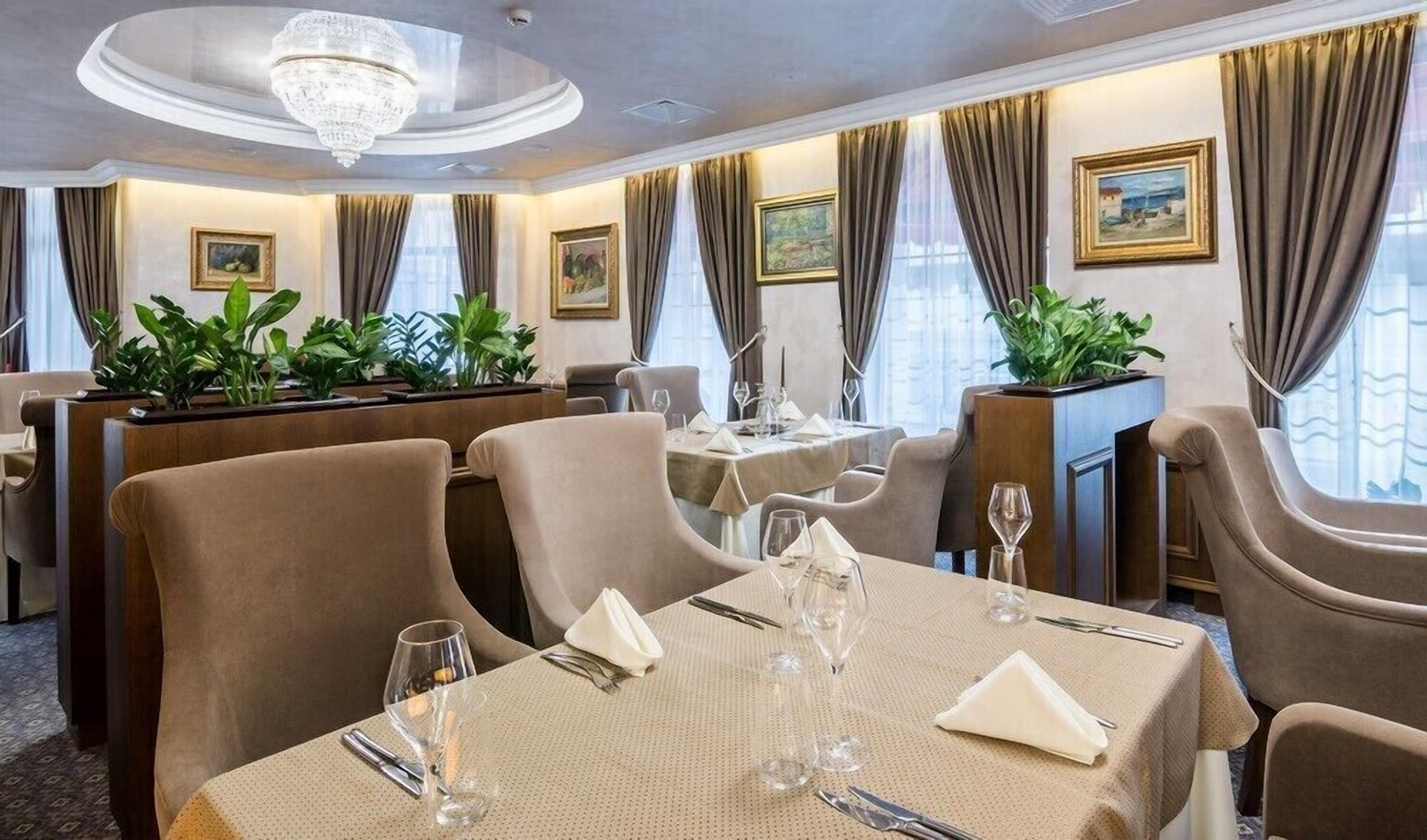 A formal dining room with tables set for four, elegant chairs, and a chandelier.