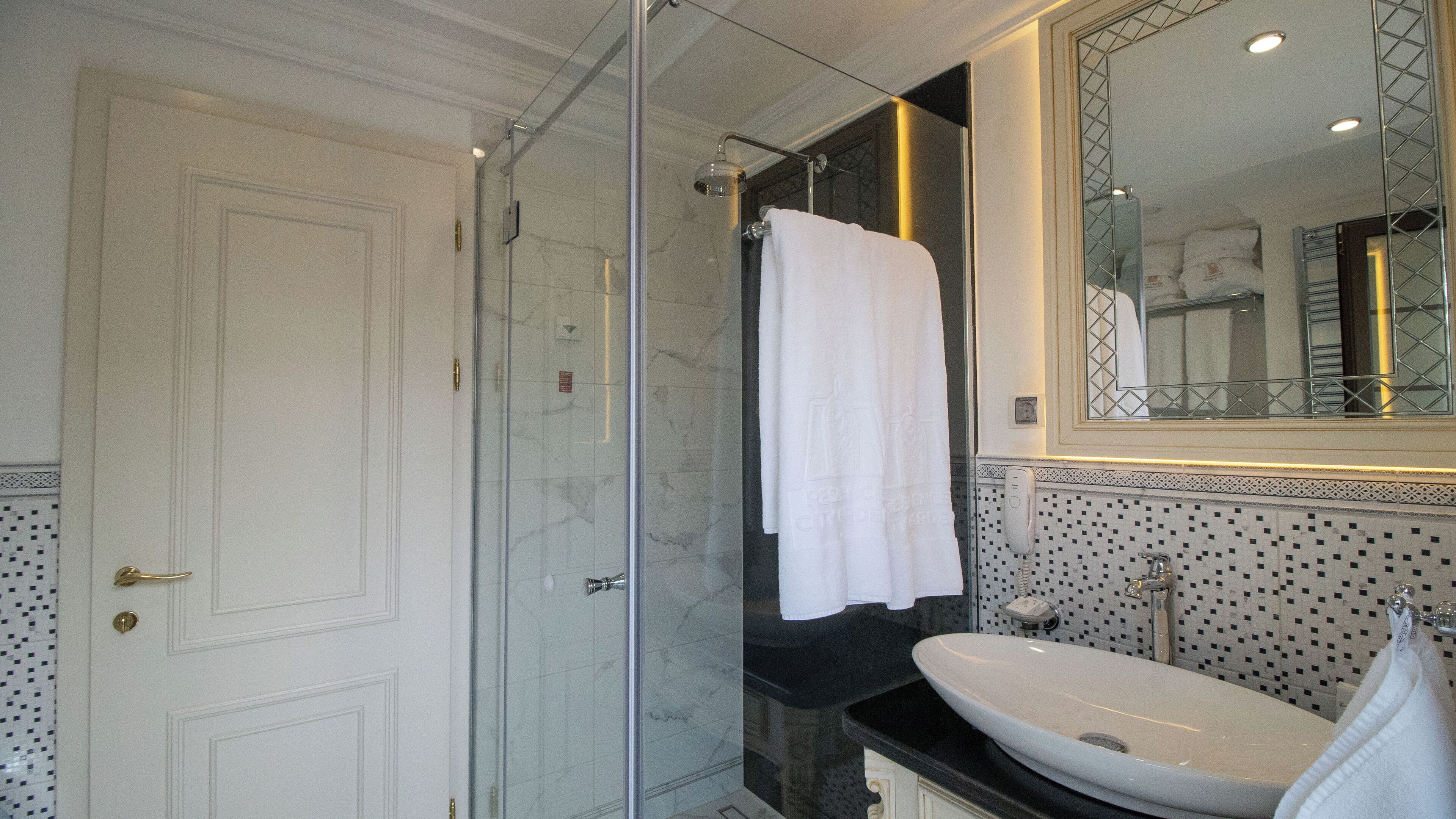 Een moderne badkamer met een douchecabine van glas, een grote spiegel en een witte wastafel.