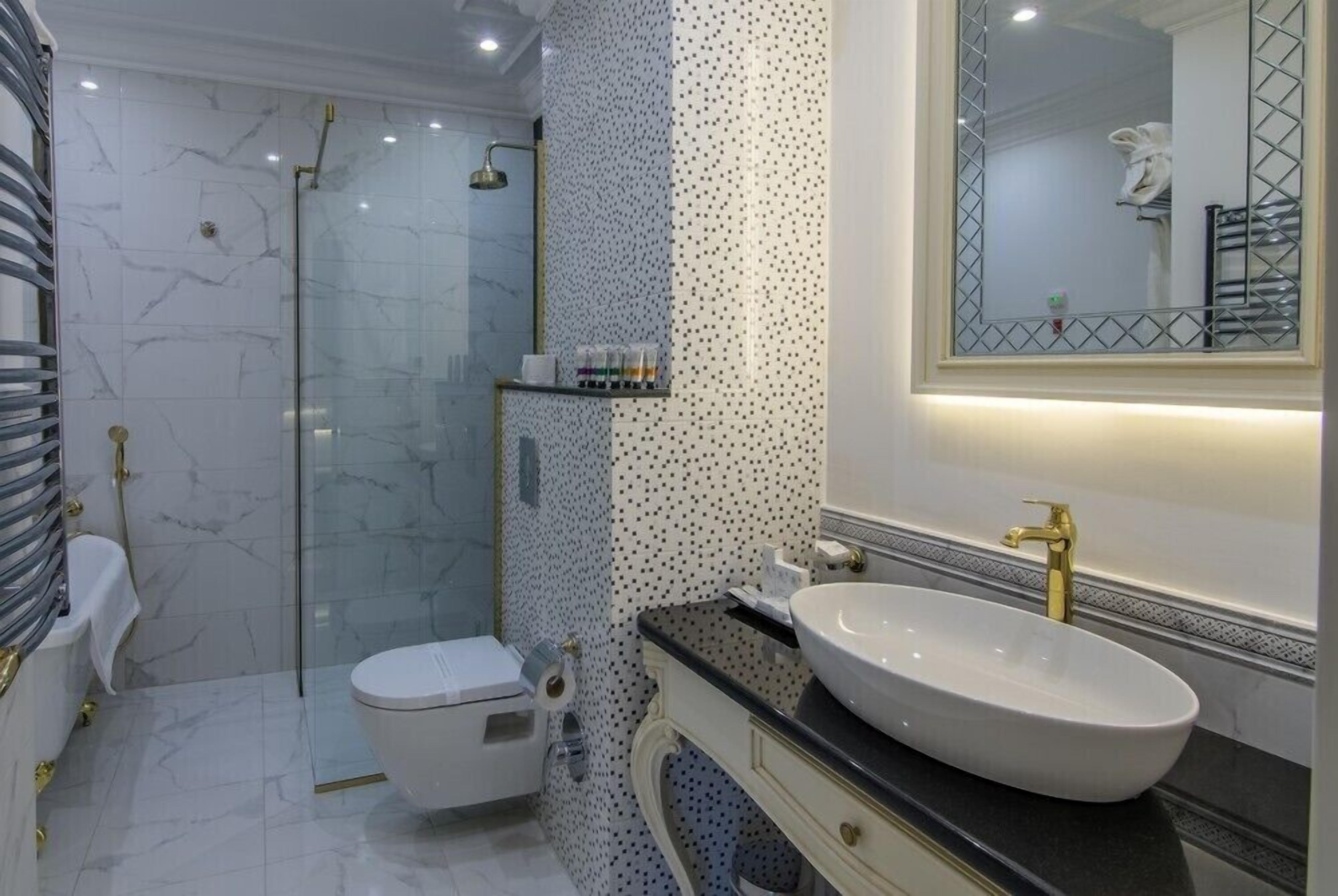 Un baño moderno con ducha de vidrio, inodoro blanco, tocador con un lavamanos grande y un espejo con marco decorativo.