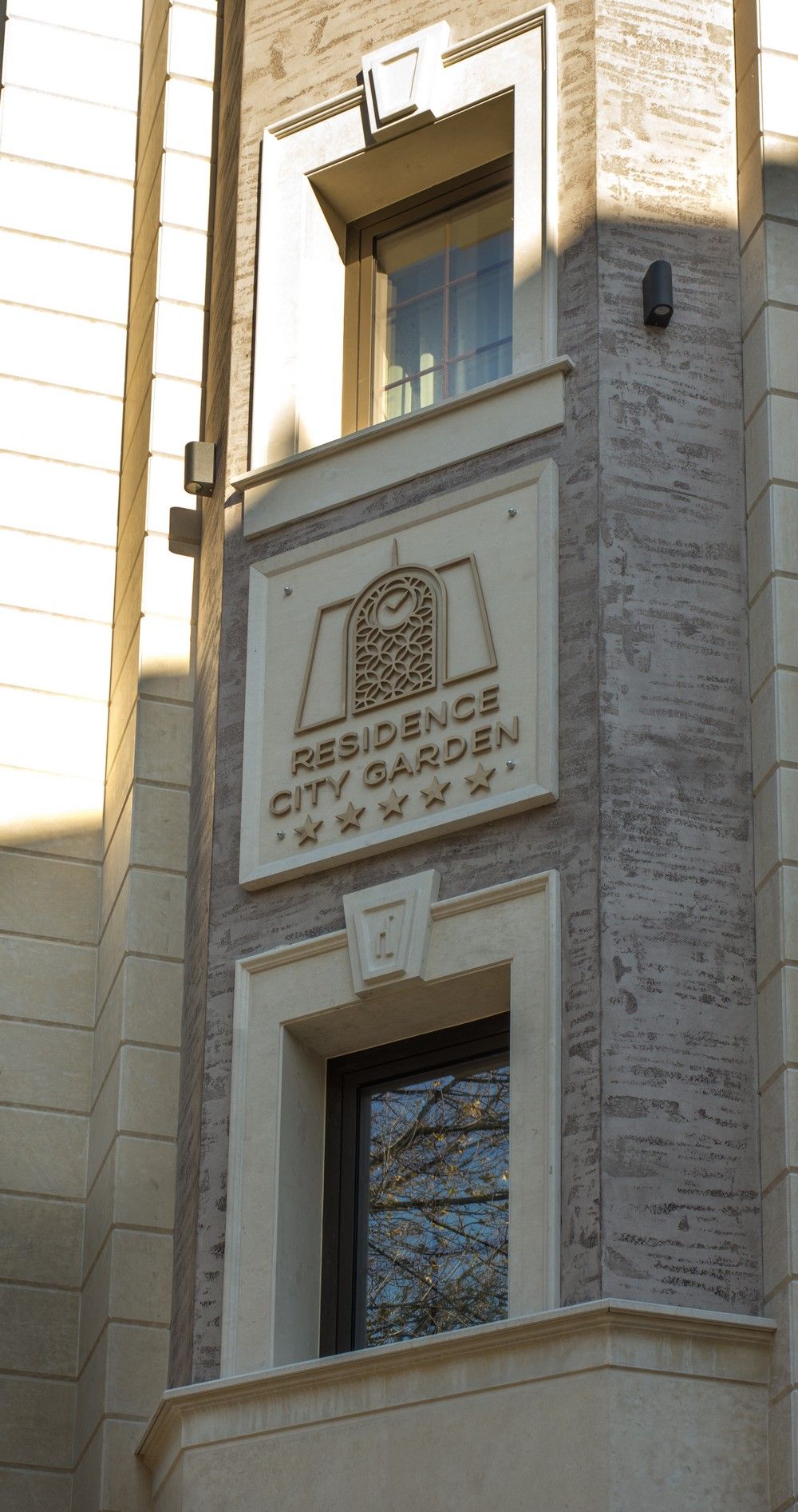 Fachada de un edificio con un cartel que dice 'Residence City Garden' y una ventana con vista a árboles.