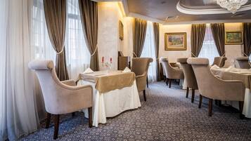A dining area with a table set for four, surrounded by upholstered chairs, a patterned carpet, and draped curtains.