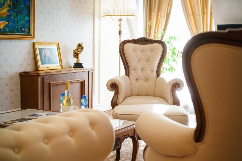 A well-lit room with a large armchair, a small table with a bottle, and a framed picture on a cabinet.