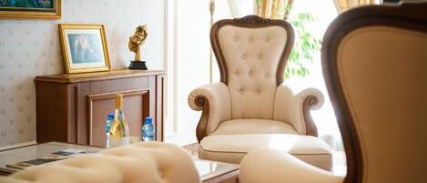 A well-lit room with a large armchair, a small table with a bottle, and a framed picture on a cabinet.
