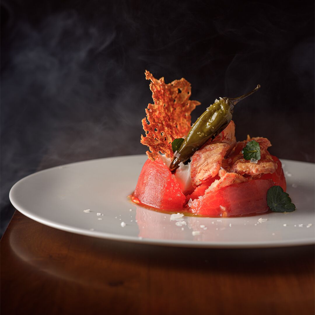 A dish with a red base, green garnish, and crispy elements on a white plate.