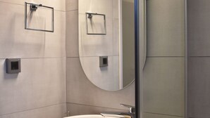 Un baño moderno con un espejo ovalado grande, un lavabo blanco y un pequeño estante con un jabonera.