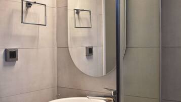 A modern bathroom with a large oval mirror, a white sink, and a small shelf with a soap dish.