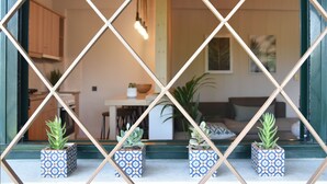 Vista a través de una ventana con diseño de rombos y cuatro macetas con plantas frente a una cocina y zona de estar.