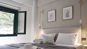 Una cama bien hecha con un edredón a rayas blanco y gris, un sombrero blanco y dos cuadros en la pared.