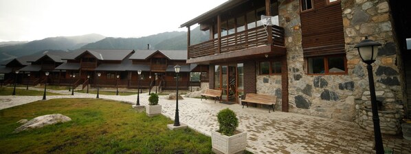 Un hotel con varias cabañas de madera, muros de piedra y un patio empedrado con bancos y plantas en macetas.