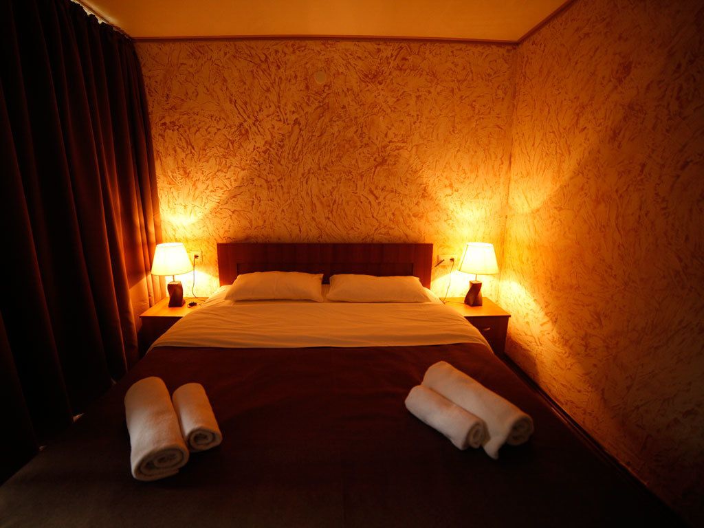 A hotel room with a large bed, two bedside lamps, and rolled towels on the bed.