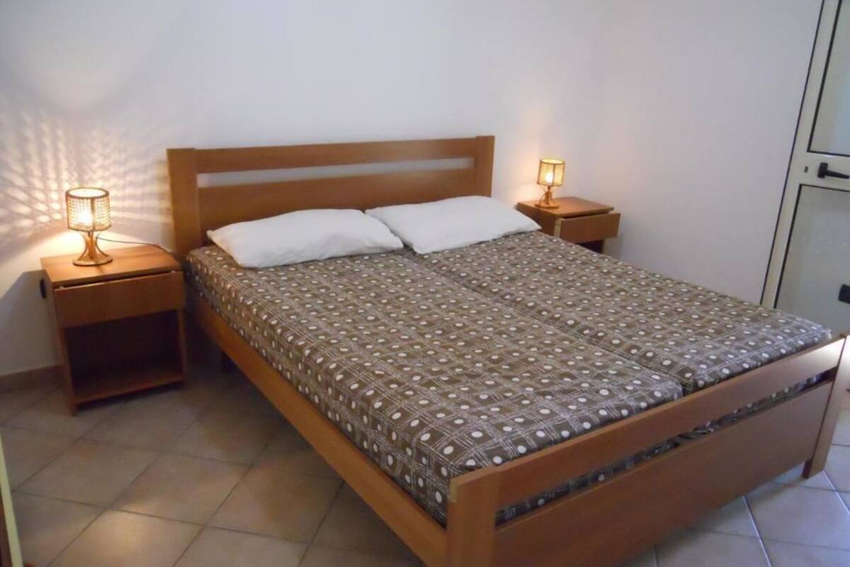 Un lit simple avec une couvre-lit à motifs, deux tables de chevet avec des lampes et une tête de lit en bois.