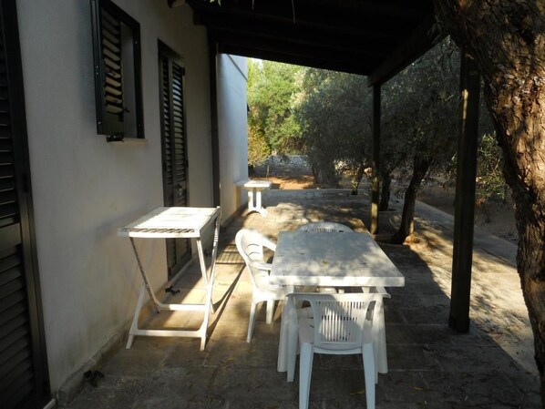 Un patio al aire libre con una mesa y sillas blancas, rodeado de muros de piedra y árboles.