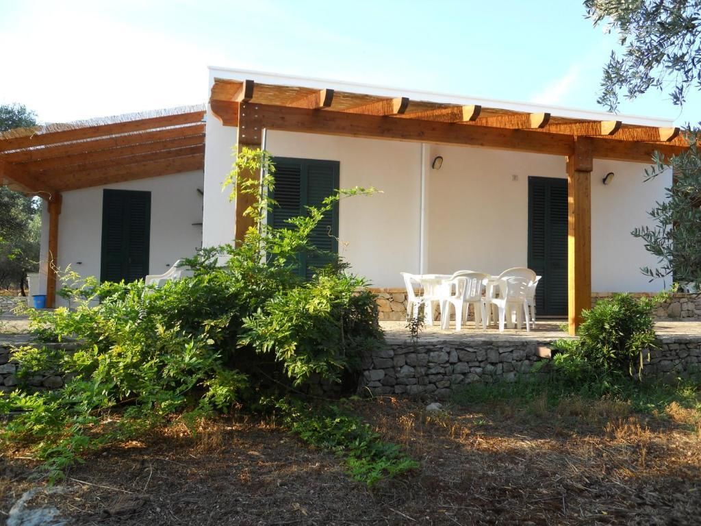 Um edifício com alpendre coberto, paredes de pedra e um pequeno jardim com arbustos verdes.
