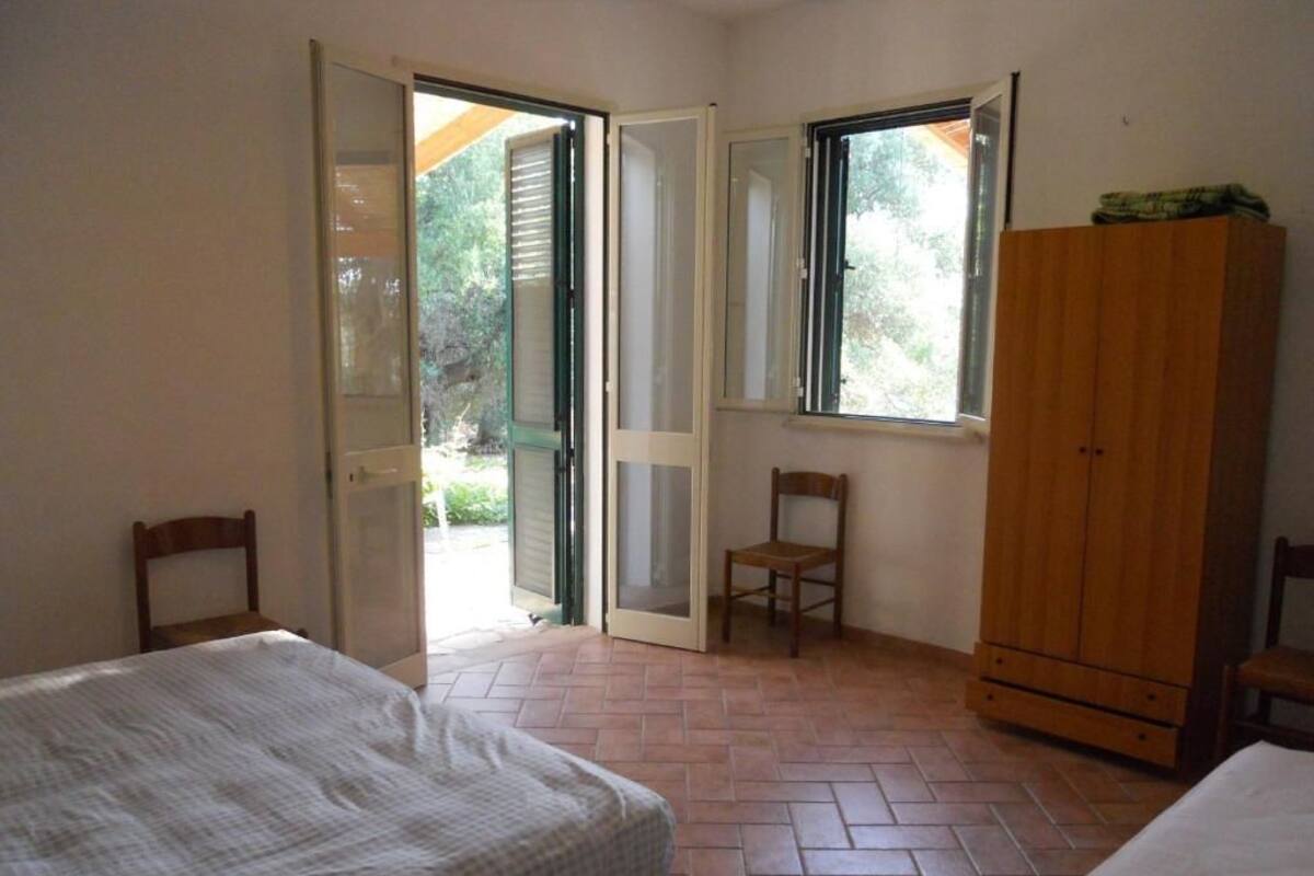 Une chambre avec deux lits, une armoire en bois et une porte-fenêtre coulissante donnant sur un espace extérieur.