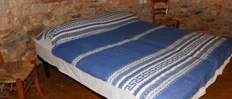Una cama individual con una colcha azul y blanca estampada en una habitación con pared de piedra y suelo de madera.