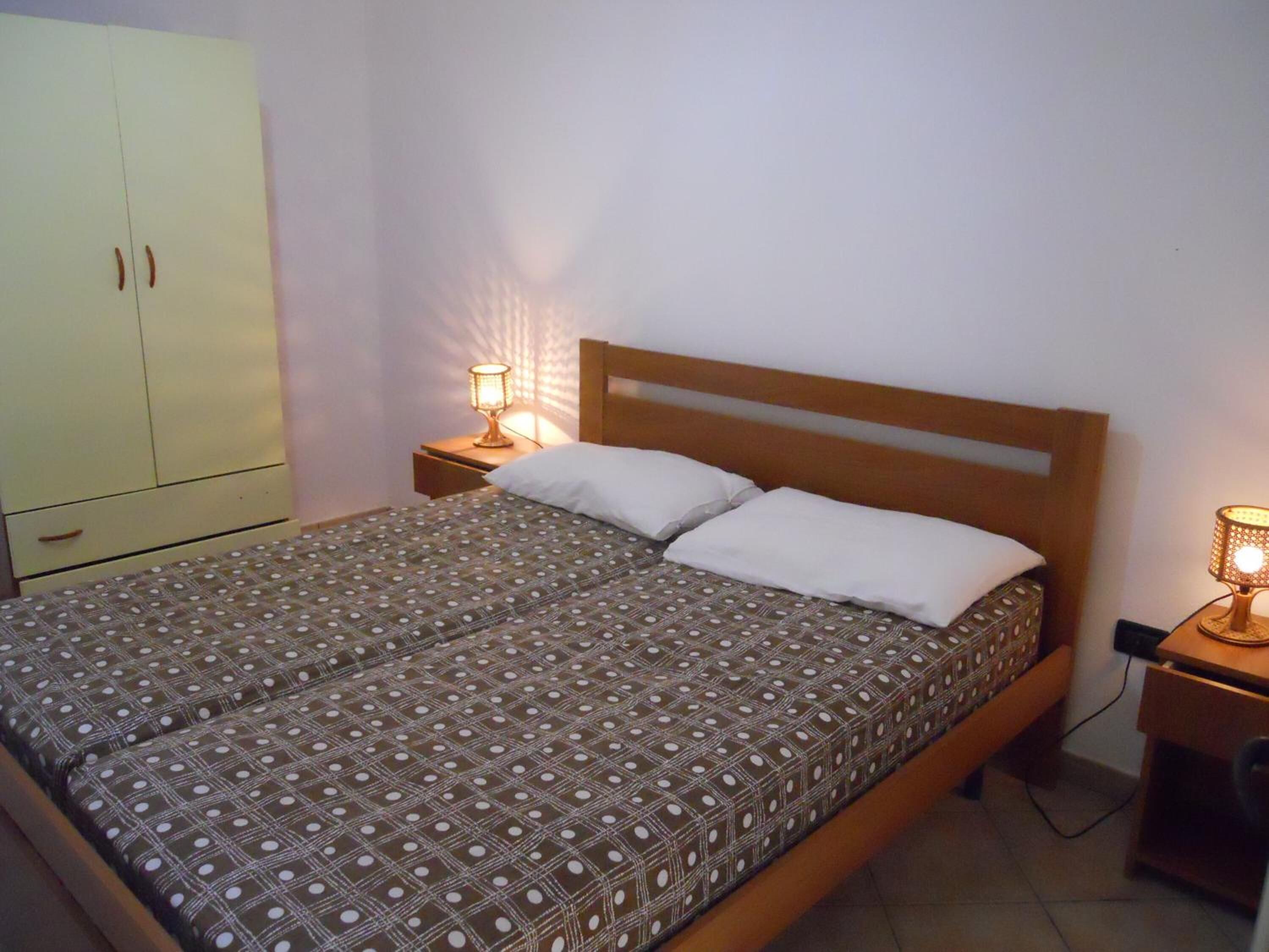 Una cama individual con una colcha estampada, dos lámparas de noche, un cabecero de madera y un armario de dos puertas.