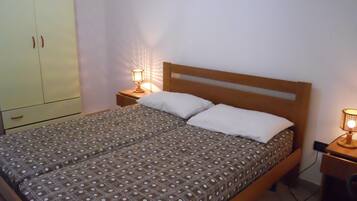 Un lit simple avec une couvre-lit à motifs, deux lampes de chevet, une tête de lit en bois et une armoire à deux portes.