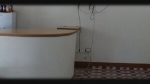 Angolo cottura con piano in legno, lavello bianco e pavimento piastrellato. Ci sono prese elettriche e una ciabatta multipresa sulla parete.