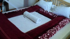 Un letto rifatto con un cuscino bianco e un asciugamano arrotolato di colore bianco.