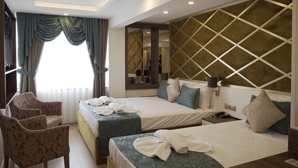 Une chambre d’hôtel avec deux lits, un coin salon avec un fauteuil, un grand miroir et un décor en bois au plafond.