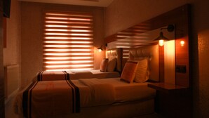 A hotel room with two beds, a large window with blinds, a bedside lamp, and a mirror on the wall. - Van Hotel (Van)