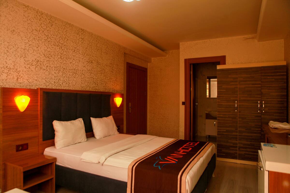Una habitación de hotel con cama, lámparas de noche, armario y escritorio.