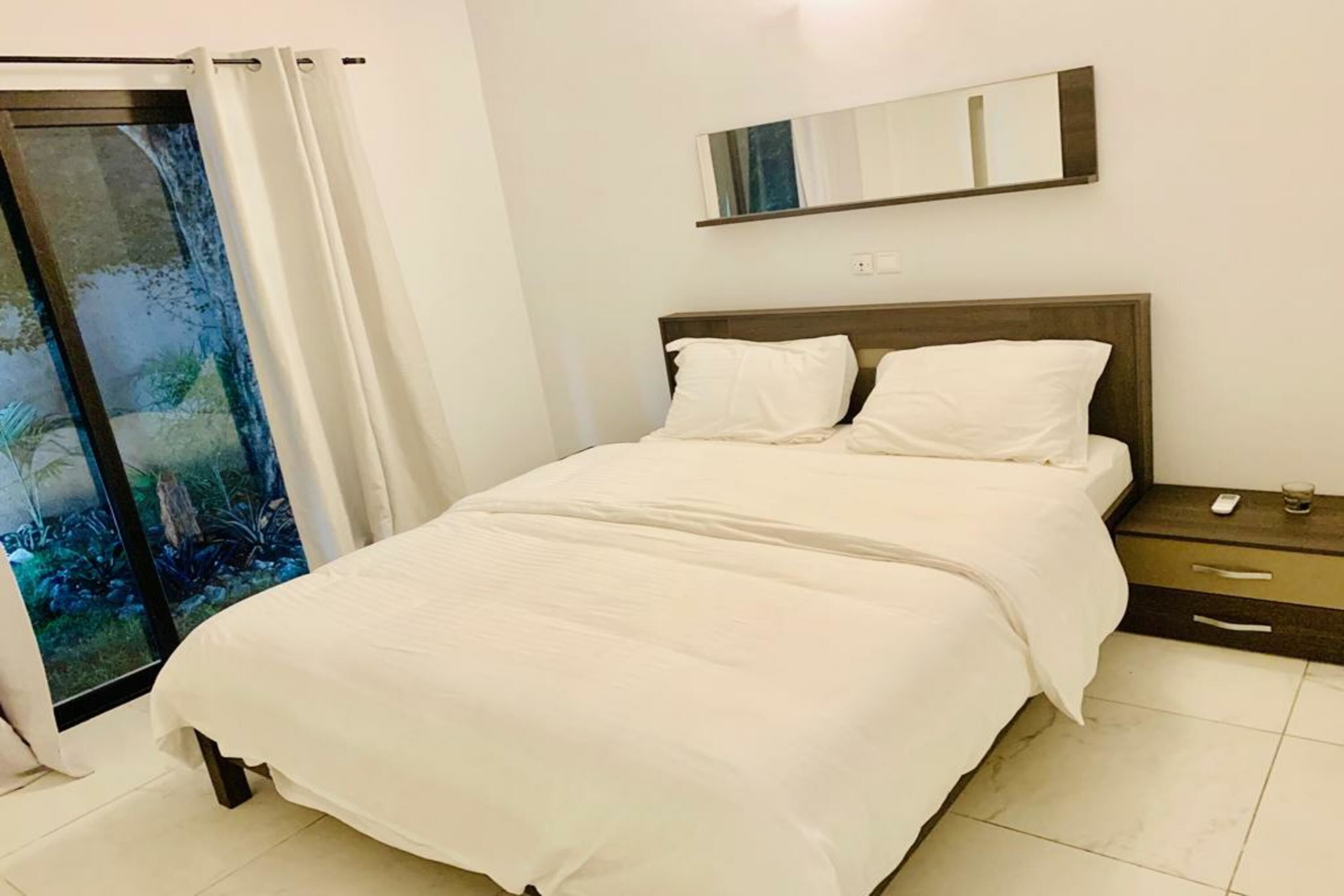 A bedroom with a bed, a nightstand, a mirror, and a sliding glass door with curtains.