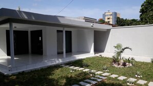 Un edificio moderno con techo plano, un patio cubierto y un pequeño jardín con piedras para pisar y plantas.