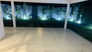 Amplio espacio interior con piso de baldosas y un mural que representa un jardín tropical con plantas iluminadas.