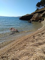 Una playa de guijarros con agua cristalina y afloramientos rocosos.