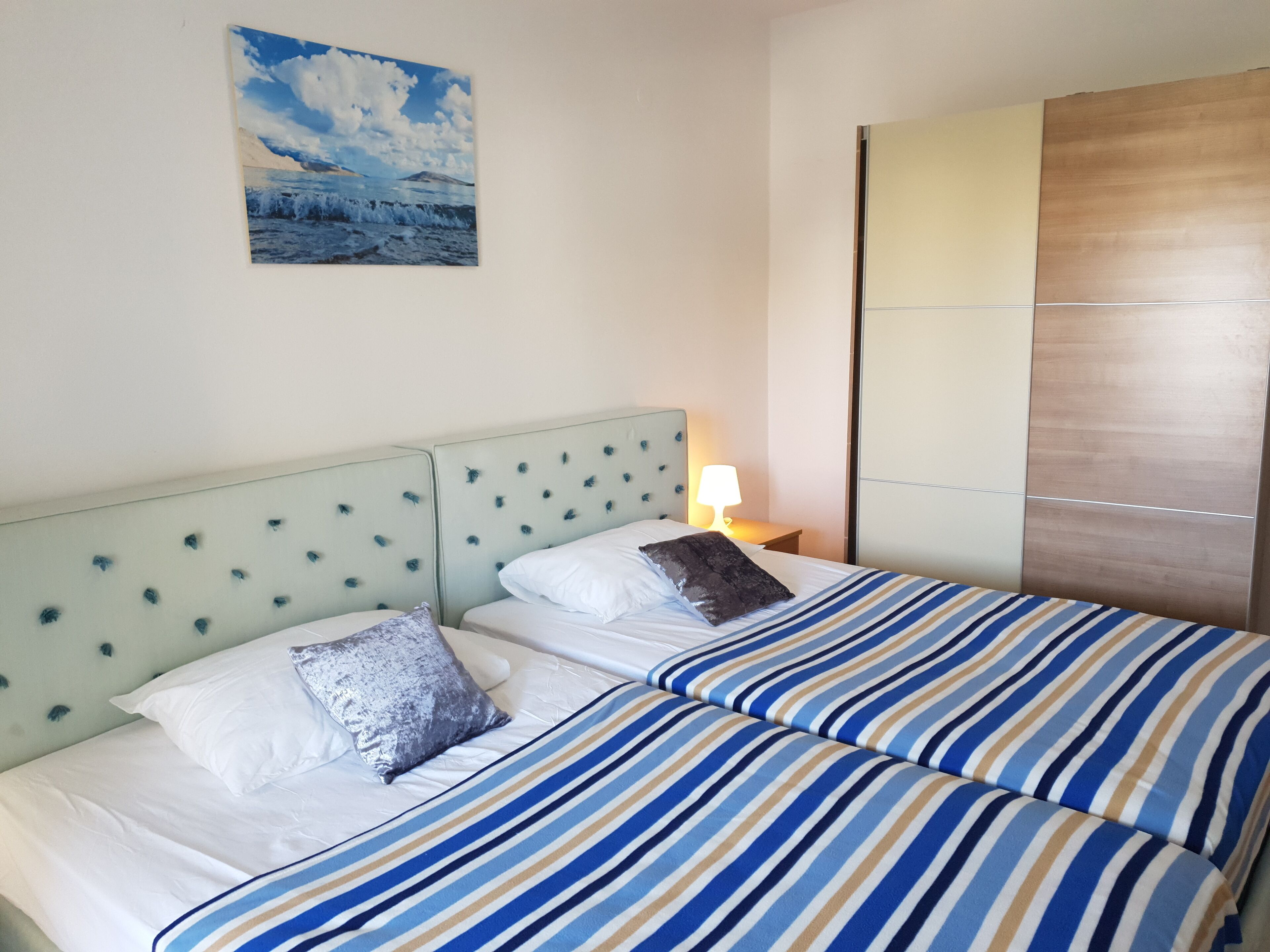 Quarto de hotel com duas camas, cabeceira com design acolchoado, pintura de paisagem e um guarda-roupa de madeira.