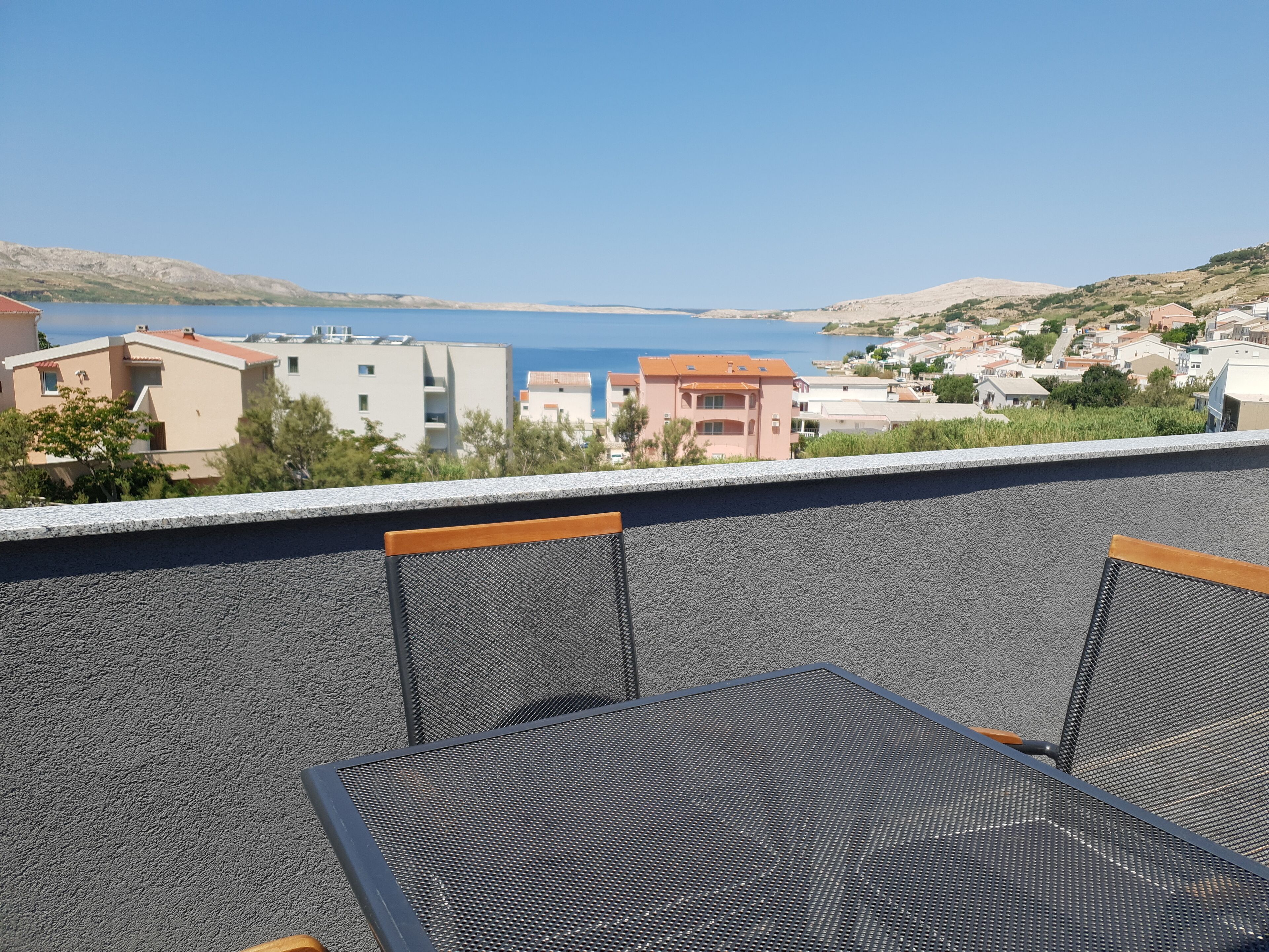 Uma varanda com vista para uma cidade costeira, com uma mesa e cadeiras.
