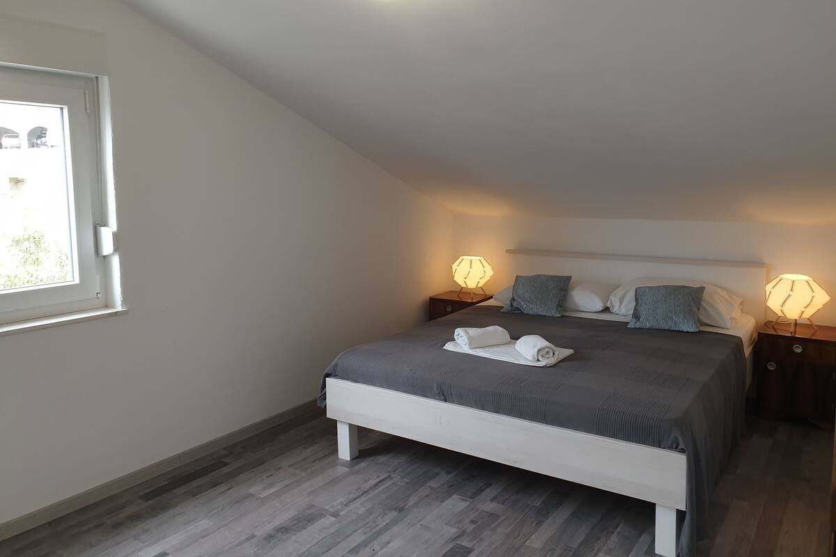 Un dormitorio con una cama, dos mesitas de noche, una ventana y una lámpara en el techo.