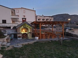 Una chimenea de piedra al aire libre con fuego, rodeada de bancos de madera y una pérgola, con vistas a una ladera.
