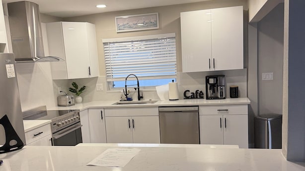 A modern kitchen with white cabinets, a stainless steel range hood, a built-in oven, and a coffee maker. - Amazing beach getaway! (Redington Beach)