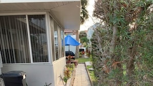 A paved pathway leading to a building with a trash bin and a blue umbrella. - Amazing beach getaway! (Redington Beach)