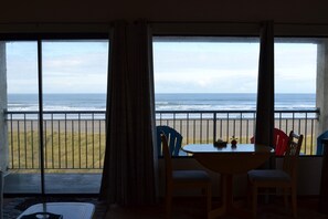 Une pièce dotée d’une grande fenêtre donnant sur la plage, d’une table avec des chaises et d’une petite table sur laquelle est posé un objet décoratif.