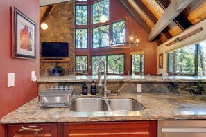 A kitchen with granite countertops, a double sink, a stone wall, a large window, and a television.