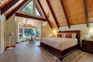 Een slaapkamer met een groot bed, houten balken in het plafond, een ventilator en uitzicht door een raam.