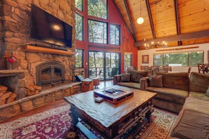 A spacious living room with a stone fireplace, large windows, a television, and a cozy seating area.
